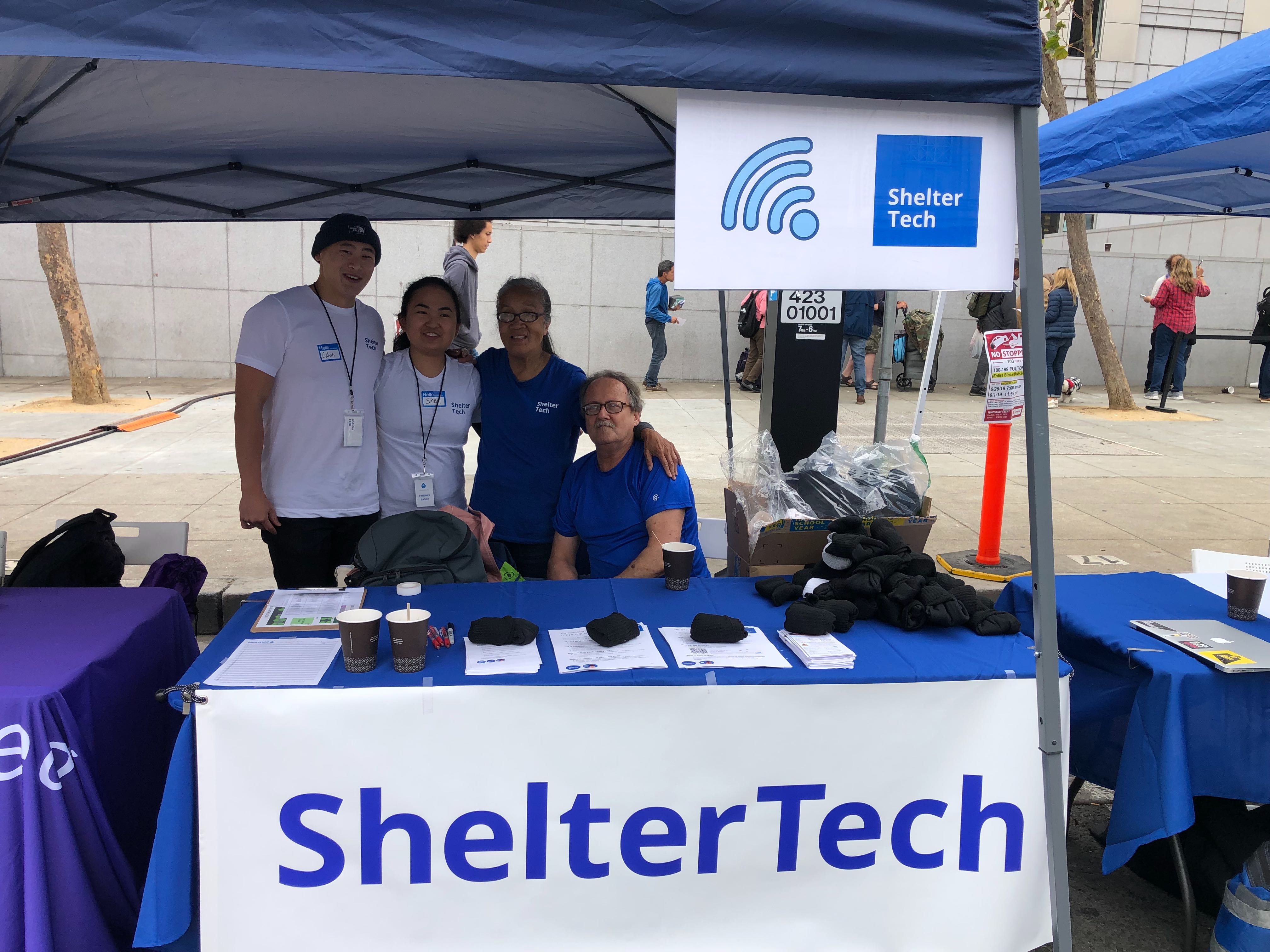 Image of ShelterTech booth with 4 volunteers smiling.